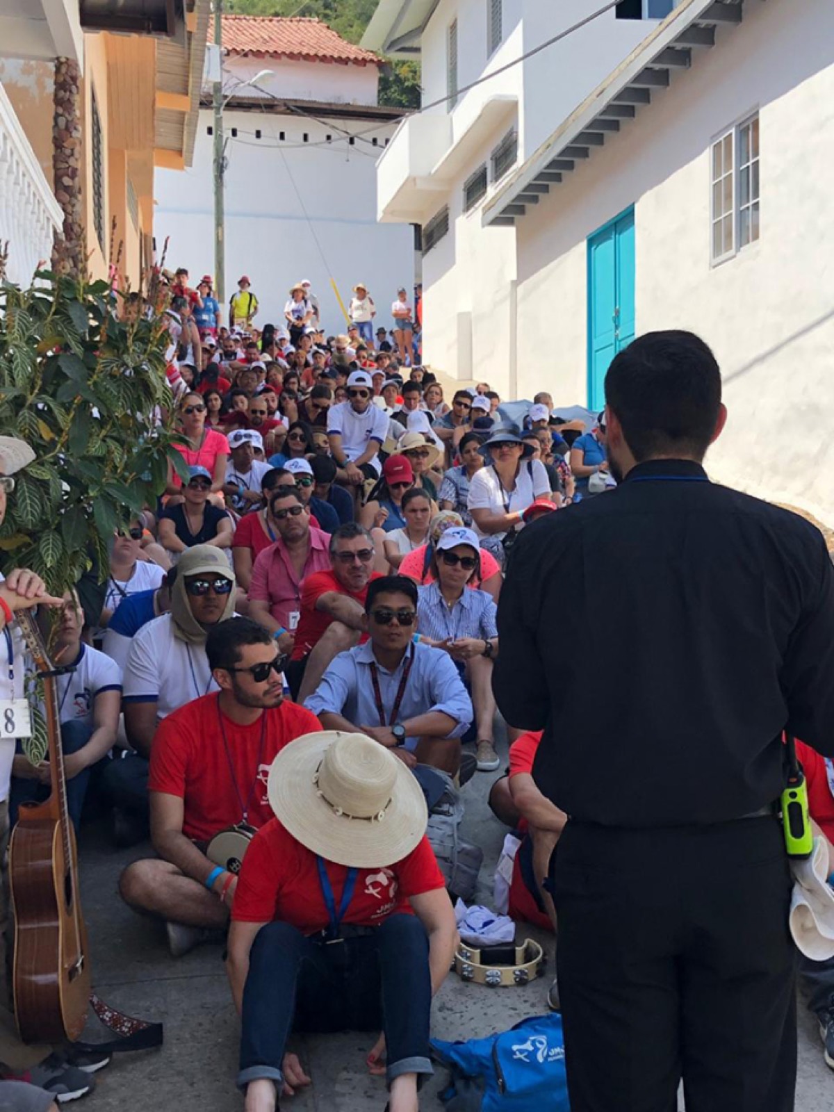 Peregrinos de la Jornada Mundial de la Juventud 2019 sentados en una calle angosta de Taboga, escuchando a un sacerdote.